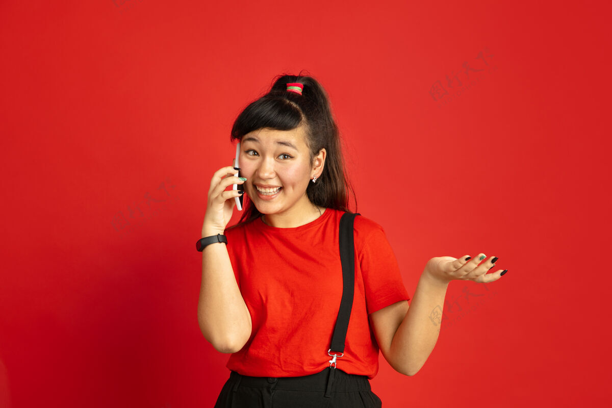 小玩意在红色工作室背景上孤立的亚洲青少年肖像美丽的深褐色女性模特 随意的长发人类情感的概念 面部表情 销售 广告电话交谈行政人员表达亚洲人