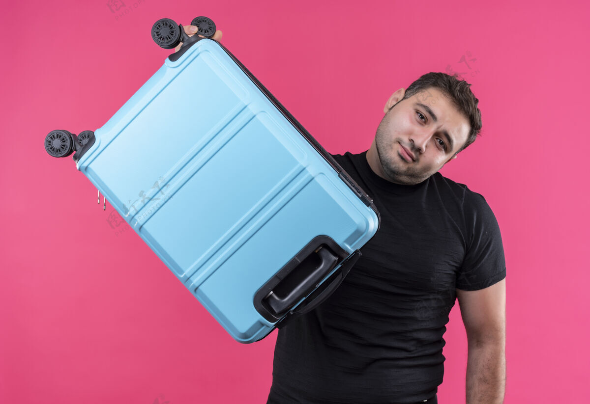 夏天穿着黑色t恤的年轻旅行家拿着手提箱站在粉红色的墙上人手提箱人