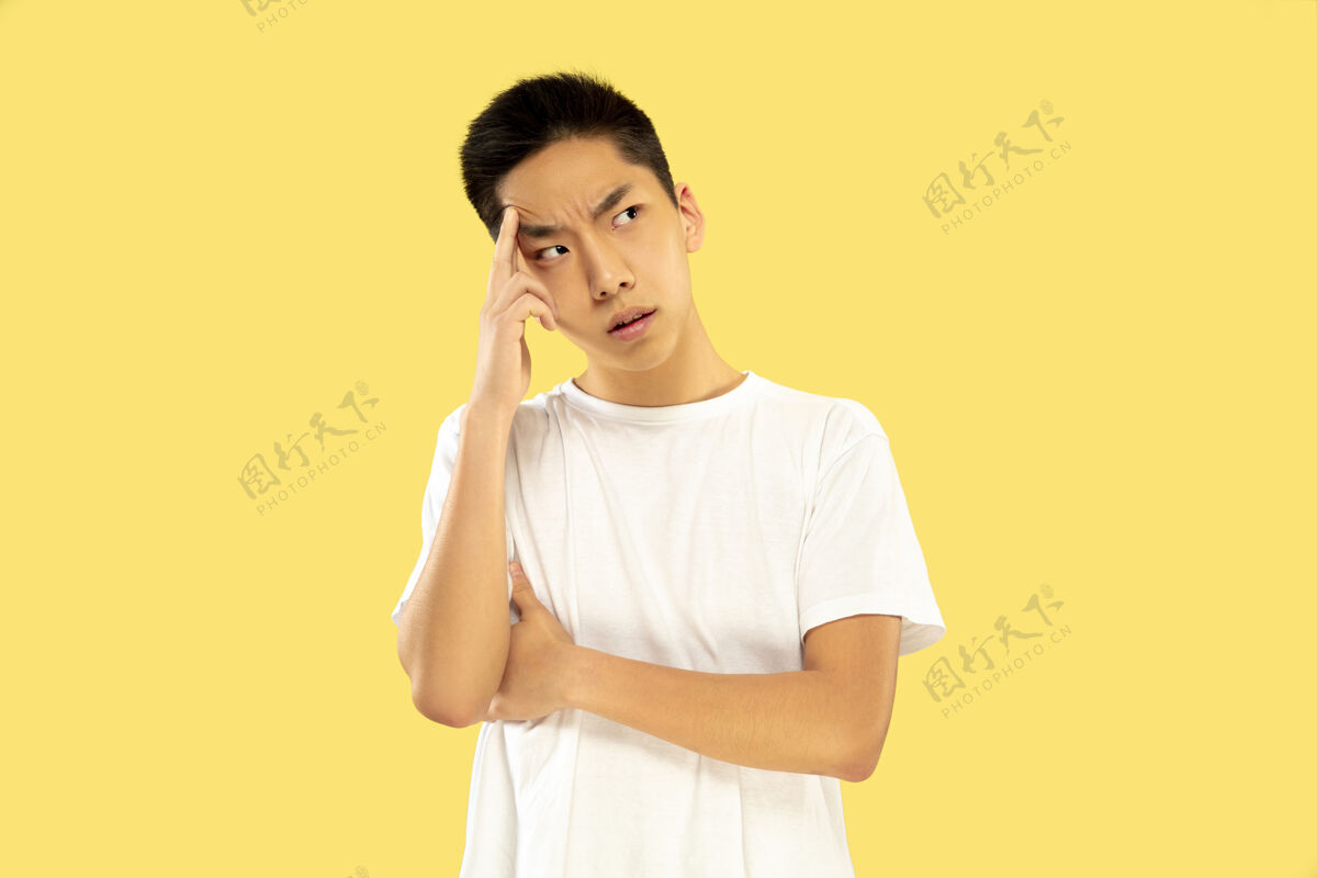 成年人黄色工作室背景上的韩国年轻人半身像穿白衬衫的男模认真思考或深思熟虑人类情感的概念 面部表情正面视图时尚色彩员工商人手势