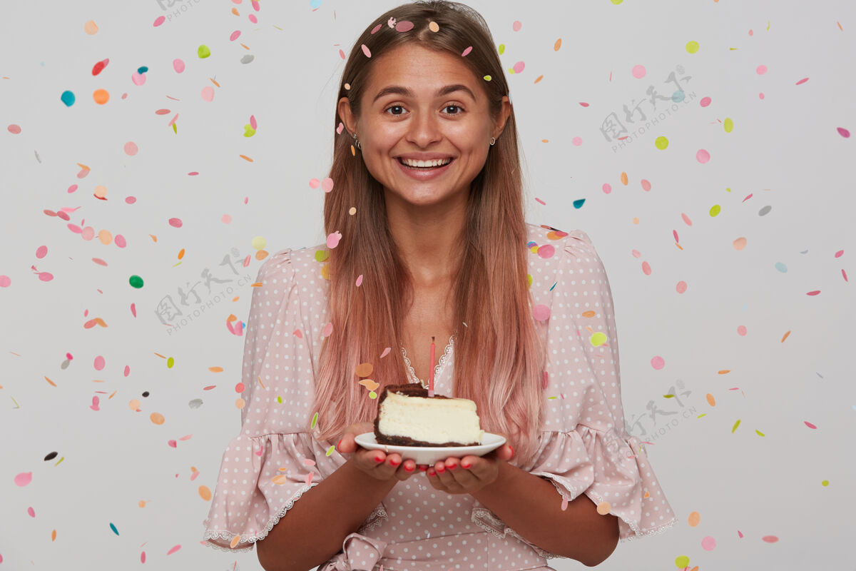 欧洲快乐的年轻可爱的女士 浅棕色的长发 拿着生日蛋糕的盘子 面带微笑 快乐地看着 隔着白色的墙优雅头发模特