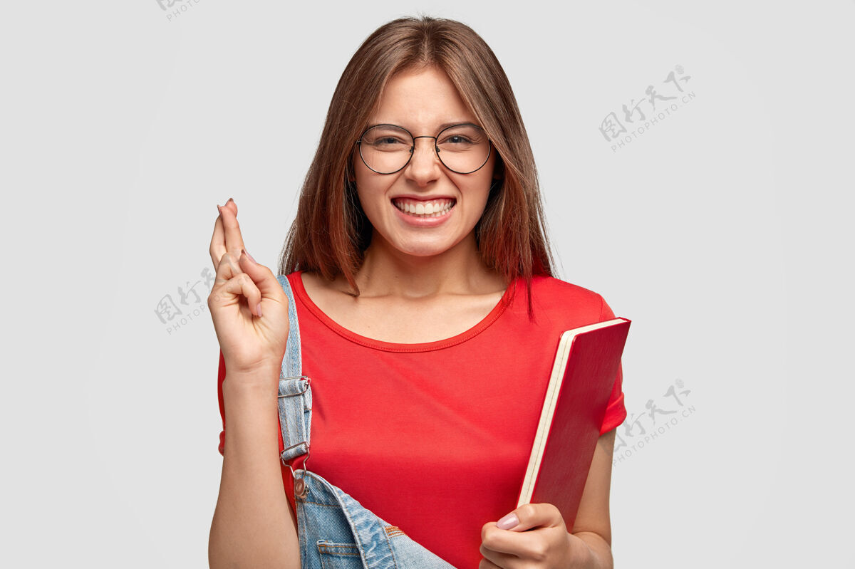 手指横拍一厢情愿的白种女人交叉手指 穿着休闲服 拿着红色课本 紧咬着牙齿 戴着圆眼镜 隔着白墙学生和欲望大学十字架室内