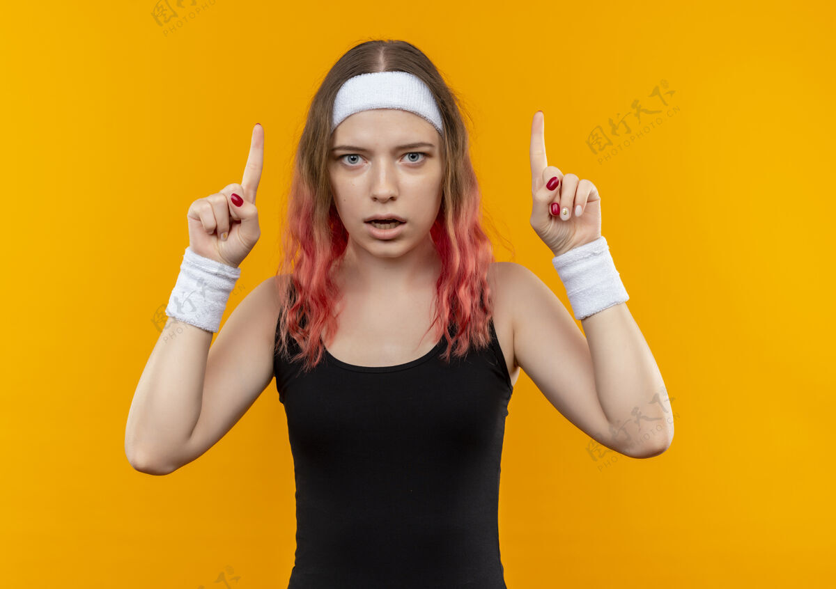 目录年轻的健身女士穿着运动服 惊讶地用食指指着站在橙色的墙上站惊喜女人