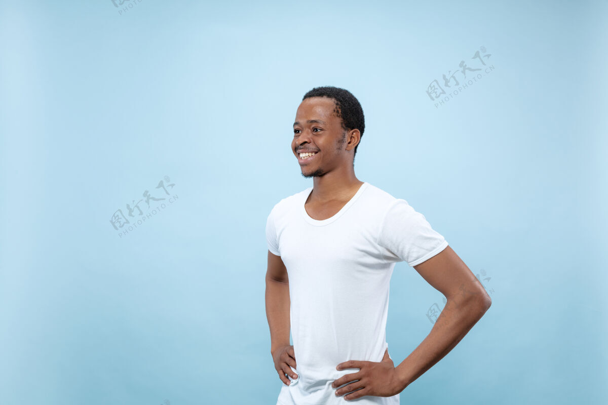 站在蓝色背景上 一位身穿白衬衫的非洲裔美国年轻人的半身特写肖像人类情感 面部表情 广告概念站立和微笑行政人员商人事业
