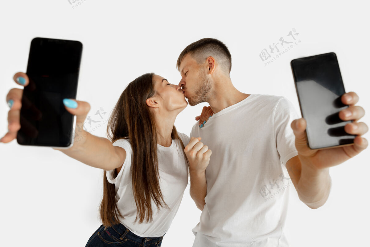 男性这对美丽的年轻夫妇的肖像被隔离在白色的工作室背景上面部表情 人类情感 广告 博彩 金融概念男人和女人拿着智能手机和屏幕惊奇肖像微笑