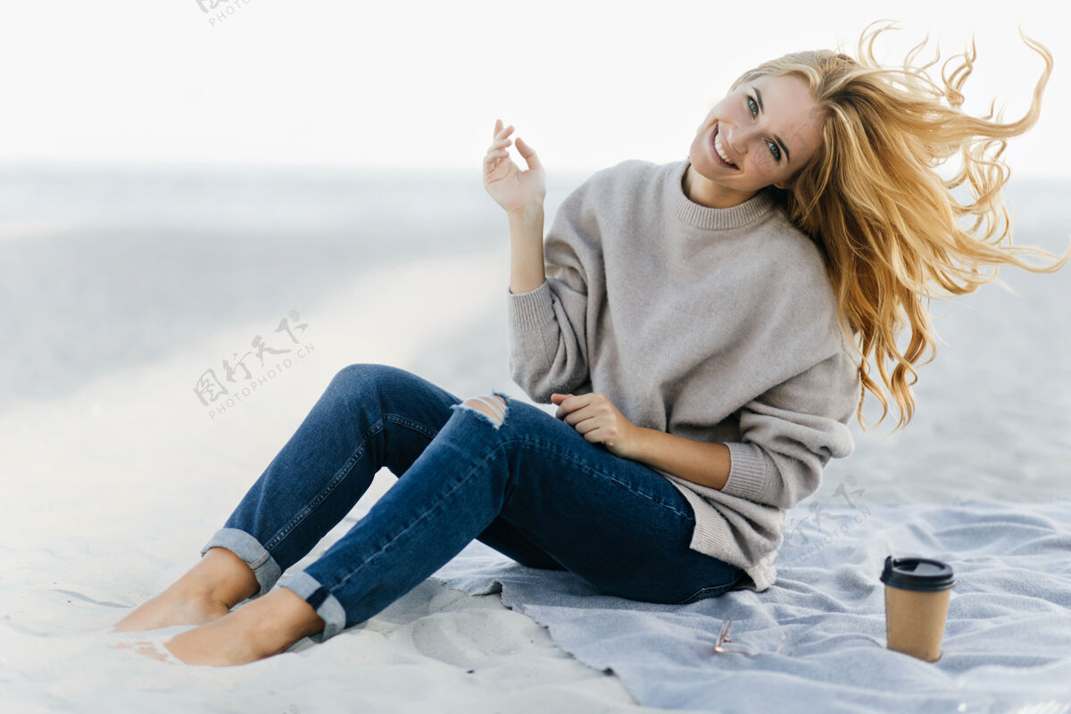 风穿着柔软毛衣的积极女人在沙滩上嬉戏迷人的女模特坐在沙滩上喝茶的户外写真自然欢呼女性