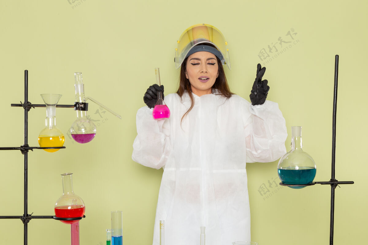 持有正面图：穿着特殊防护服的女化学家在绿色表面上拿着粉色溶液浴袍化学化学家