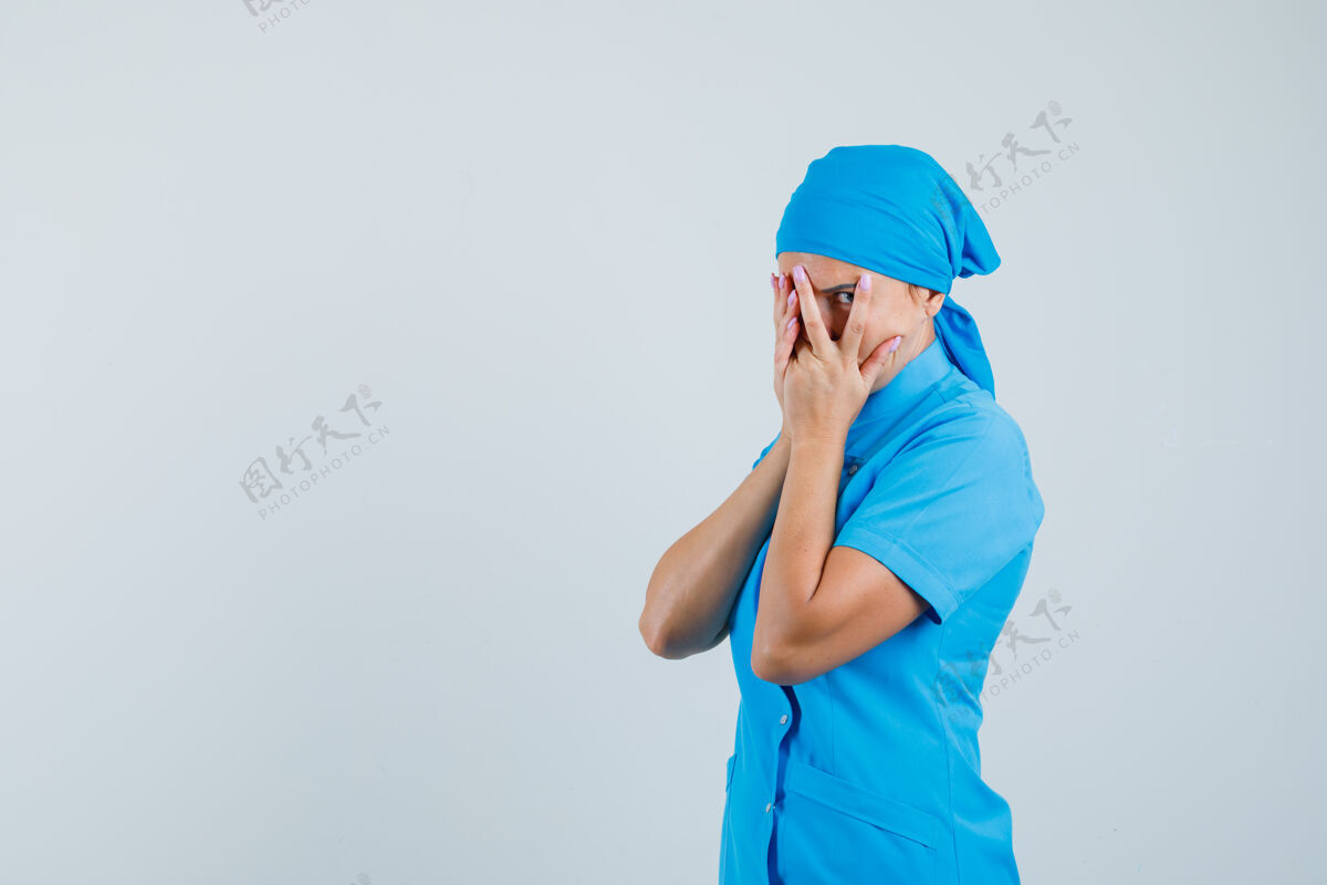 诊断女医生穿着蓝色制服 透过手指看 很好奇 前视图年轻人女人制服