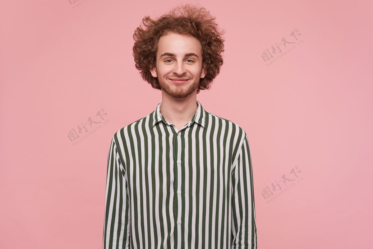 心情正面的年轻可爱的卷发红发男人的肖像 他穿着条纹衬衫 微笑着站在粉红色的墙上 双手放在身体上时尚未剃欢呼