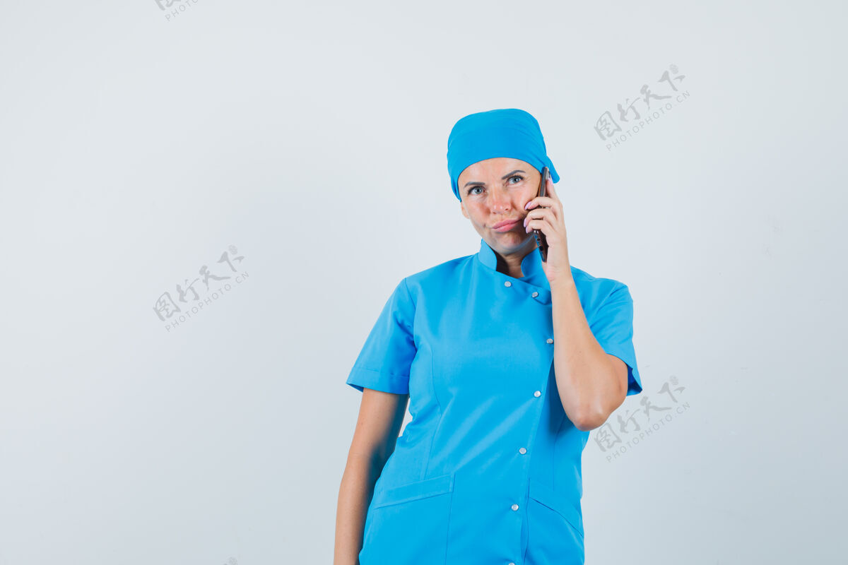 年轻人穿着蓝色制服的女医生在讲手机 神情犹豫不决 前视疾病诊所手机