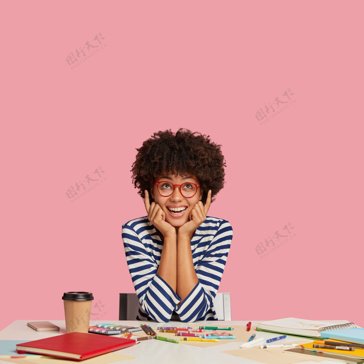 室内这是一张照片 照片拍摄的是一个有创意的年轻人 他留着非洲式发型 食指朝上 微笑着 看到了一些令人敬畏的东西 手掌放在脸颊上室内图片日记桌子记事本