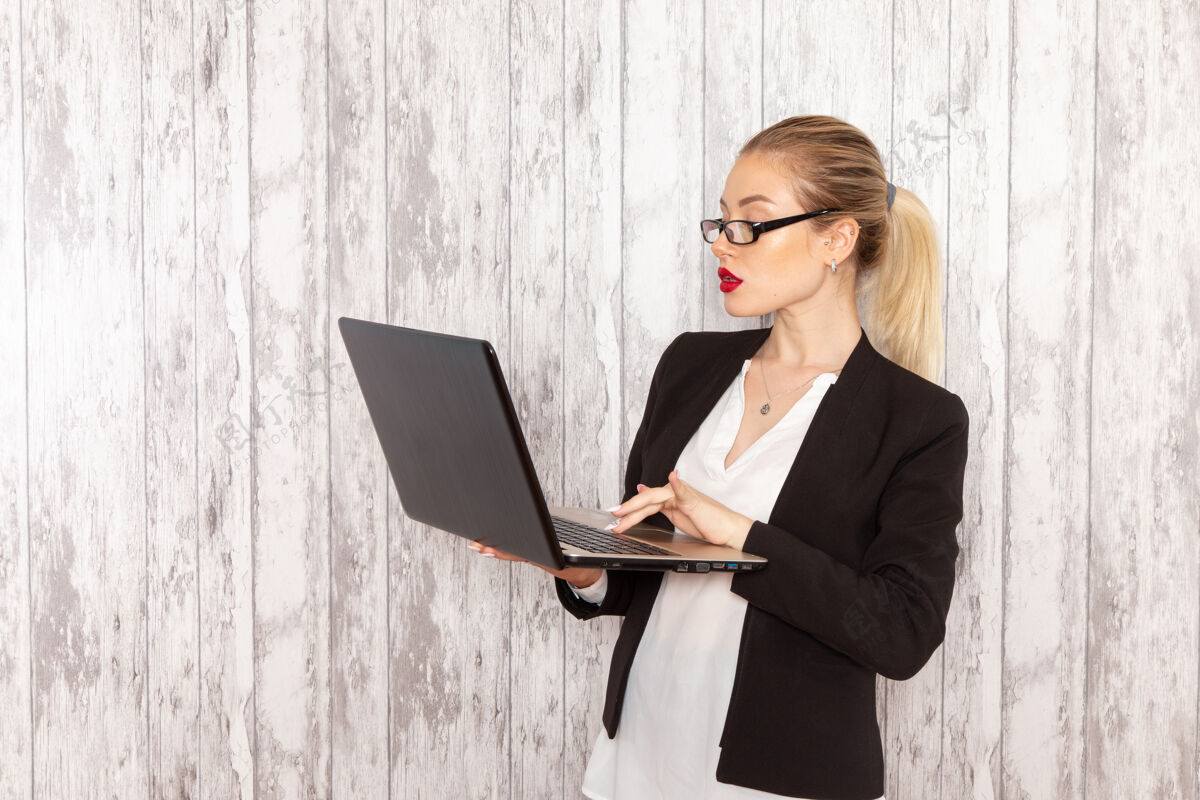 工作正面图穿着黑色夹克的年轻女商人在白色表面上使用她的笔记本电脑工作服严格女商务人士