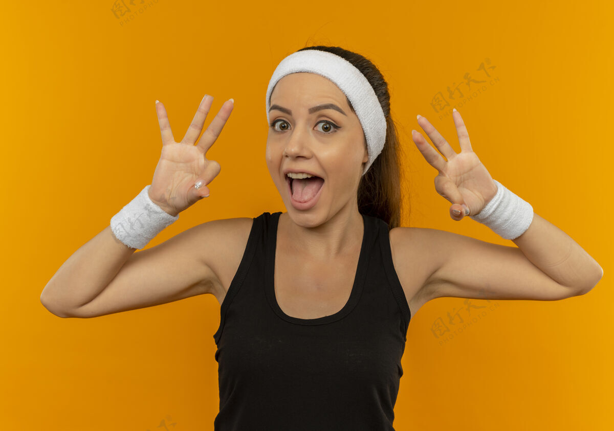 表演身穿运动服的年轻健身女 头戴花边 微笑着 乐观地站在橙色的墙上 显示“ok”的标志人市民运动