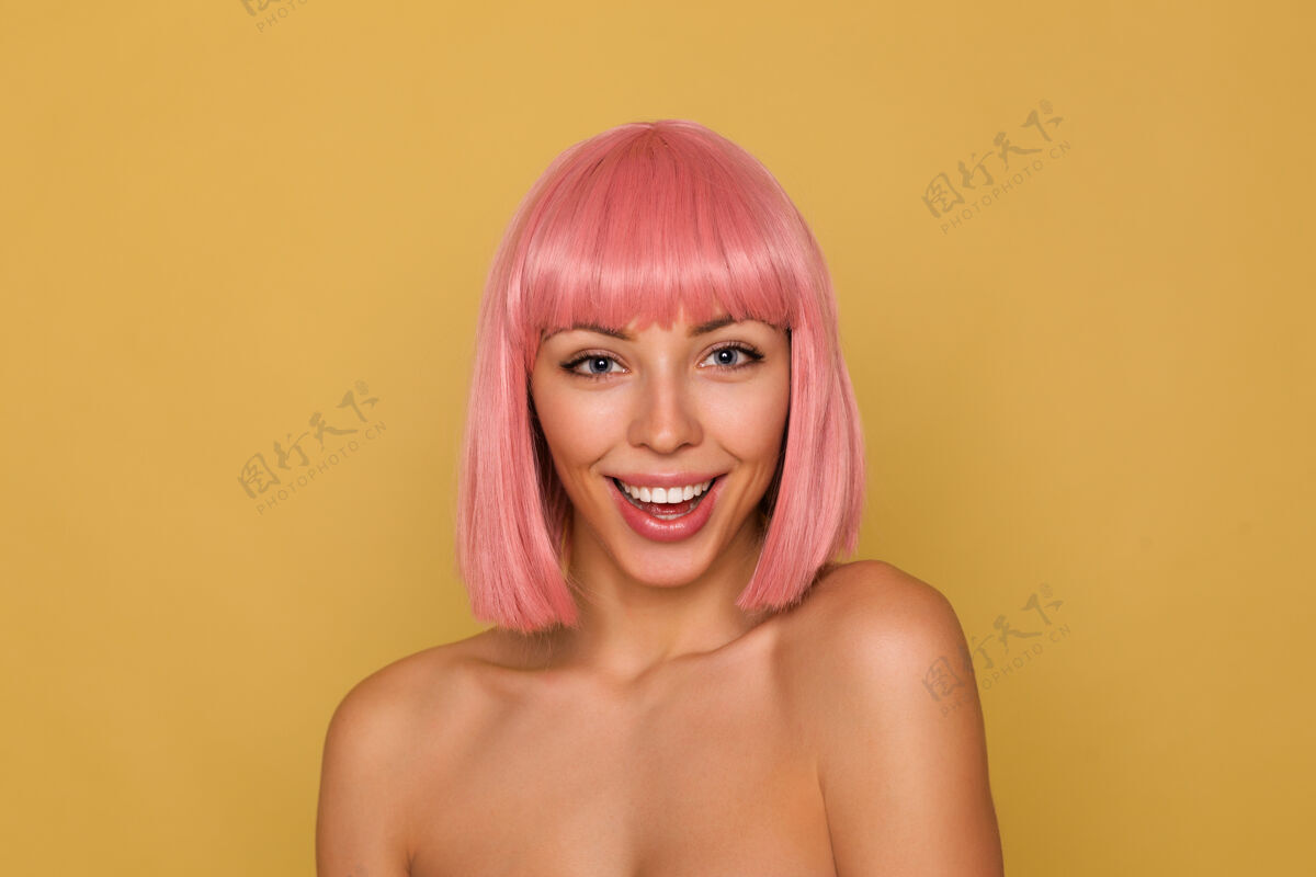 动漫一张室内照片 一位年轻漂亮的蓝眼睛粉红色头发的女士 留着鲍勃式的发型 站在芥末墙上 开心地看着相机 面带微笑女士情感发型