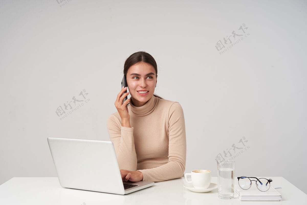 心情积极向上的年轻迷人的黑发女士 身着正装 坐在桌旁 手提电脑 手放在键盘上 愉快的通话 真诚的微笑坐着正式女士
