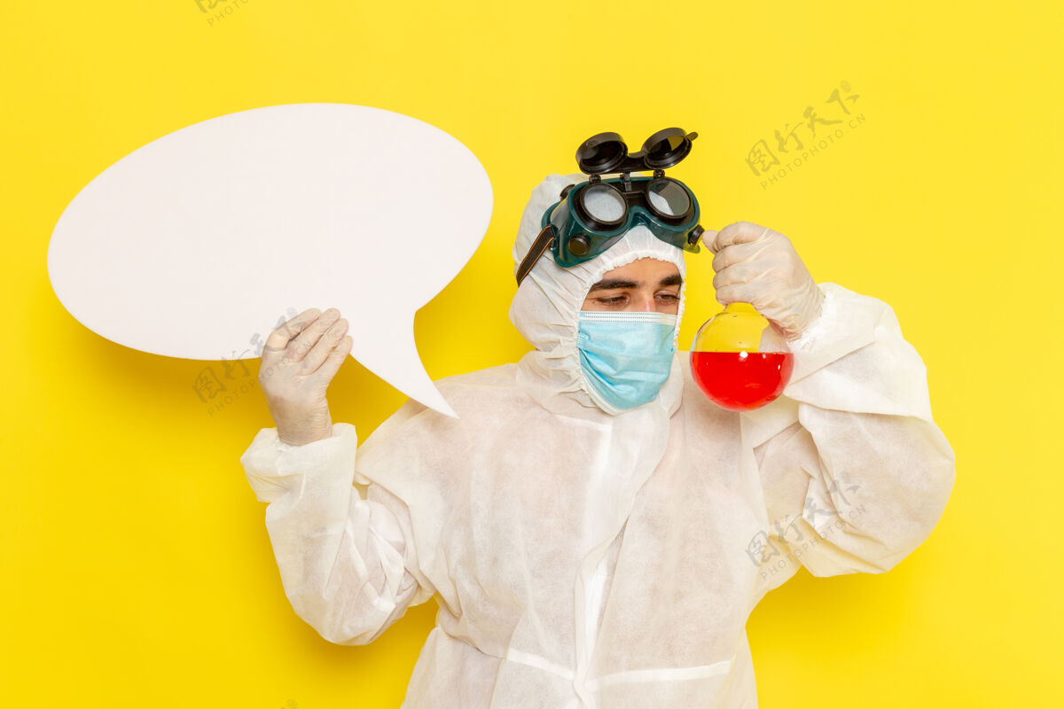腹部正面图：穿着特殊防护服的男性科学工作者 手持淡黄色桌子上的红色溶液和白色标志的烧瓶服装桌子男性