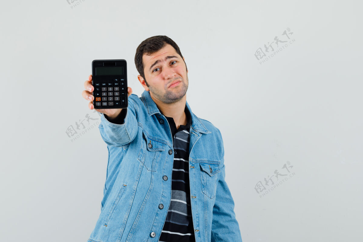 夹克年轻人展示了一个穿着t恤衫 夹克衫 看起来绝望的计算器 正面视图肖像休闲男性