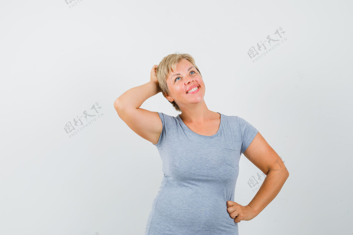 年轻金发女人把手放在腰上 想着什么 穿着浅蓝色t恤向上看 神情沉思前视图思考腰成人