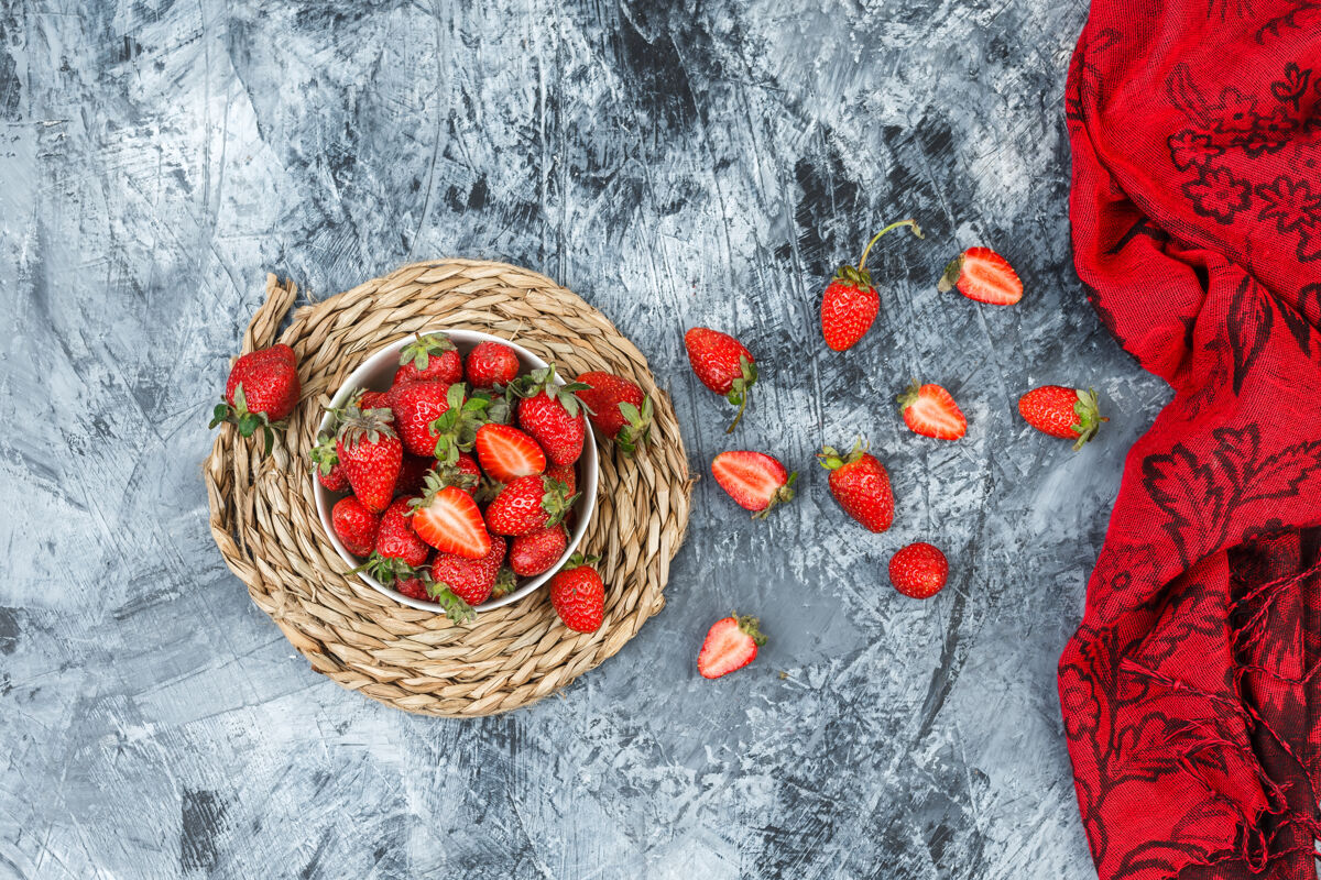 新鲜顶视图一碗草莓放在圆形柳条垫子上 深蓝色大理石表面有红领巾水平有机柳条甜点