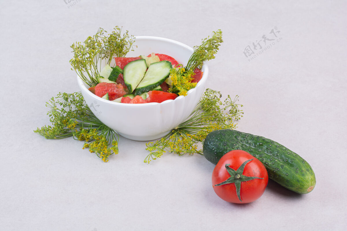 碗黄瓜和西红柿沙拉 白色表面有绿色蔬菜光滑剁碎番茄