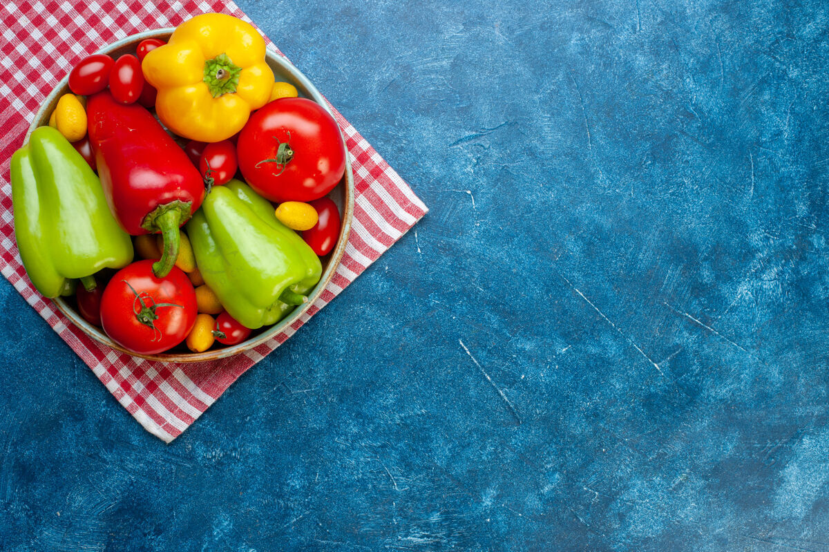 胡椒顶视图新鲜蔬菜樱桃西红柿不同颜色甜椒西红柿孜然在盘子上红色和白色格子厨房毛巾在蓝色桌子上与复制空间樱桃新鲜蔬菜风景