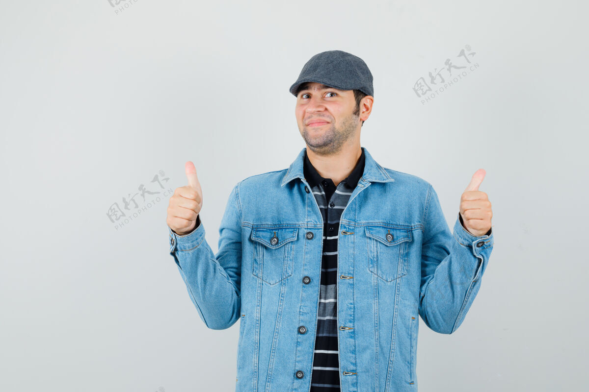 展示年轻人穿着夹克 戴着帽子 竖起大拇指 看上去很高兴正视图时尚男人男性