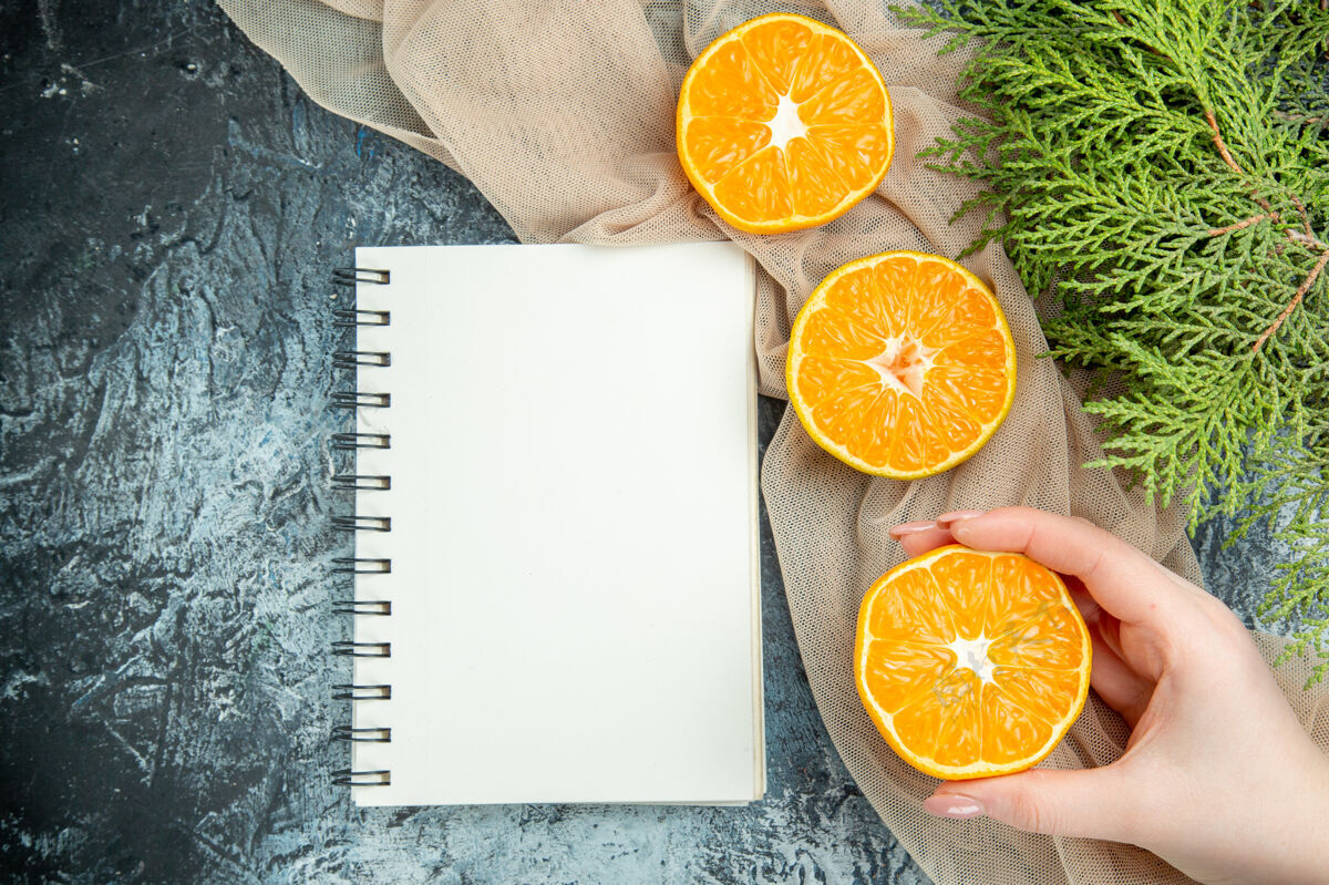 水果俯视图切割橘子在女性手松果在米色披肩记事本在黑暗的表面维生素柠檬观点