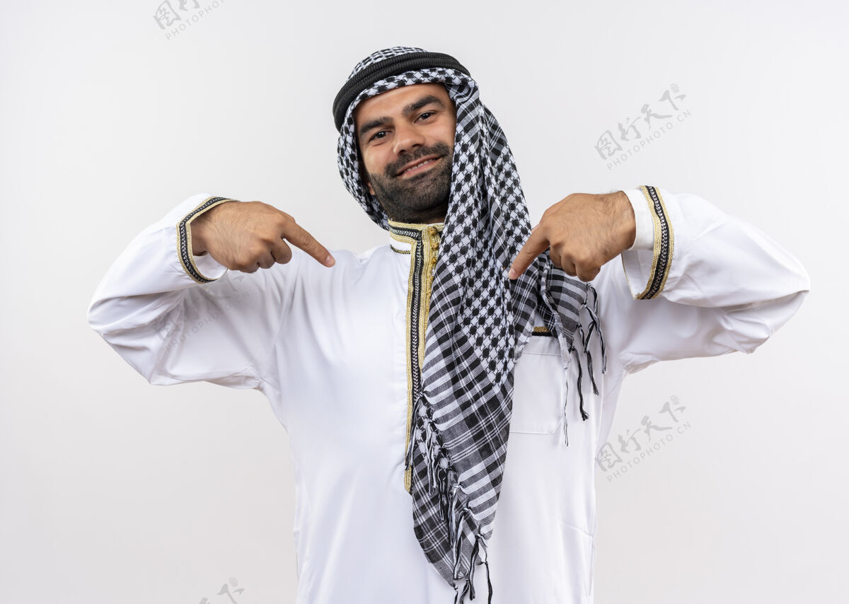 自满一个穿着传统服装的阿拉伯男人站在白墙上 用手指着自己 自鸣得意 自豪穿着站着骄傲