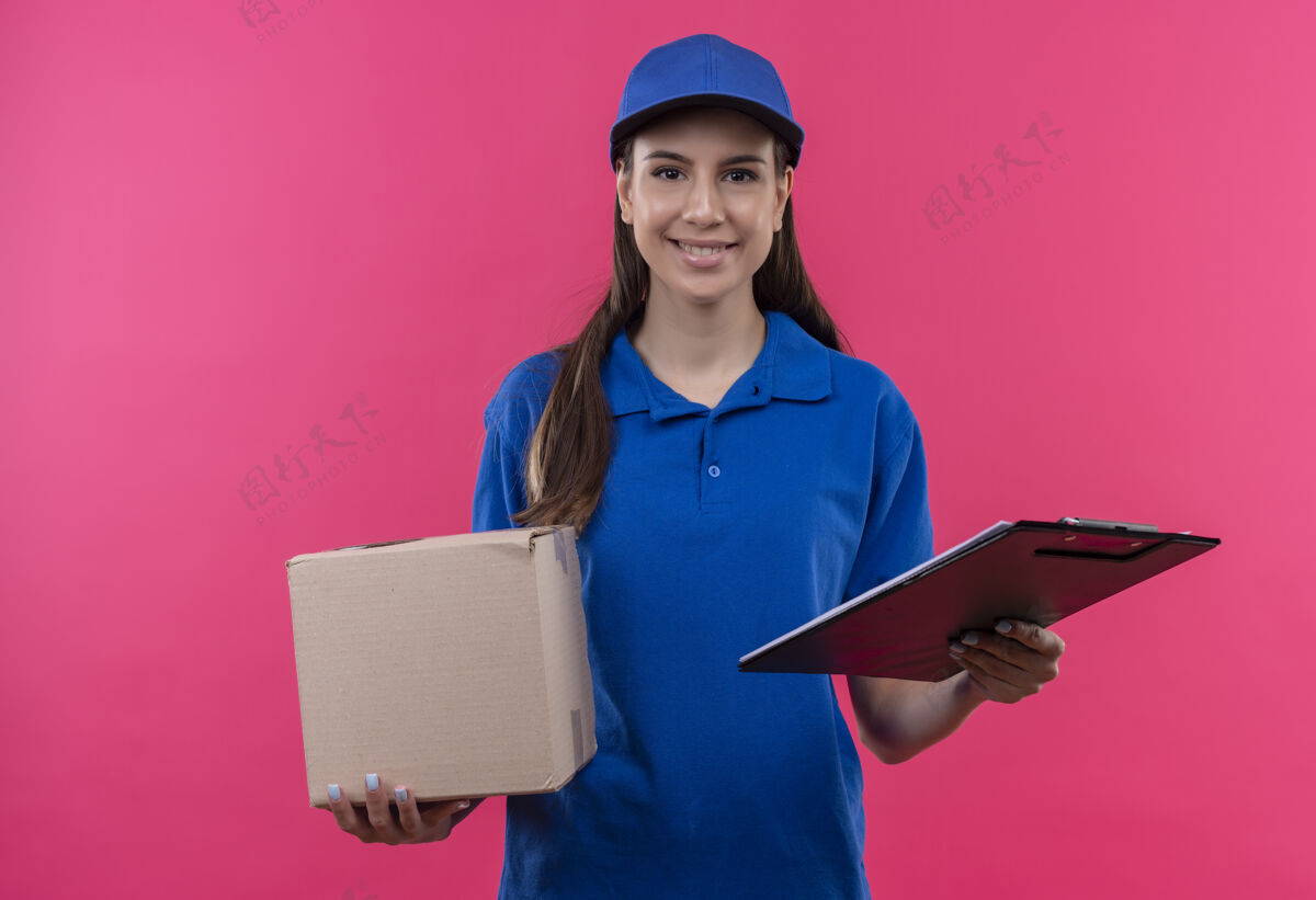 盒子年轻的送货女孩穿着蓝色制服 戴着帽子 拿着盒子和剪贴板 看起来很自信年轻送货粉色