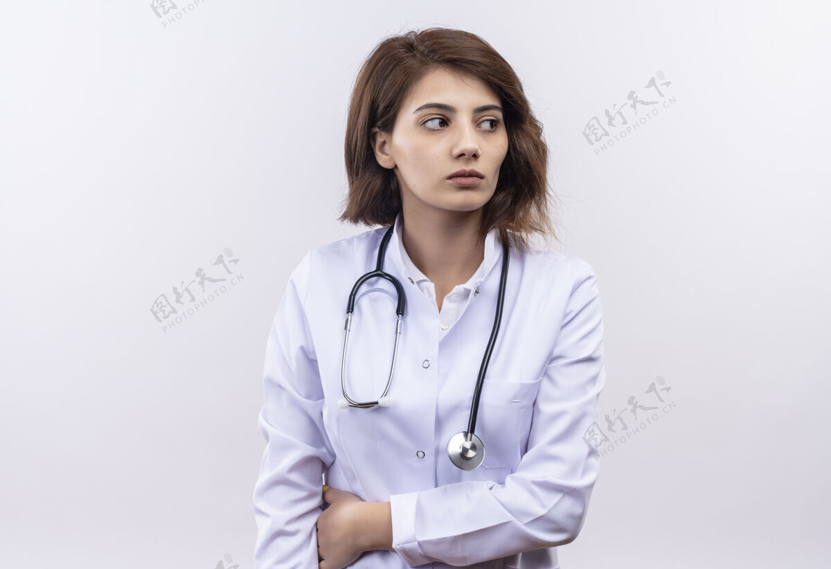 女人身穿白大褂 手持听诊器的年轻女医生表情严肃地看着一旁靠边站站着年轻