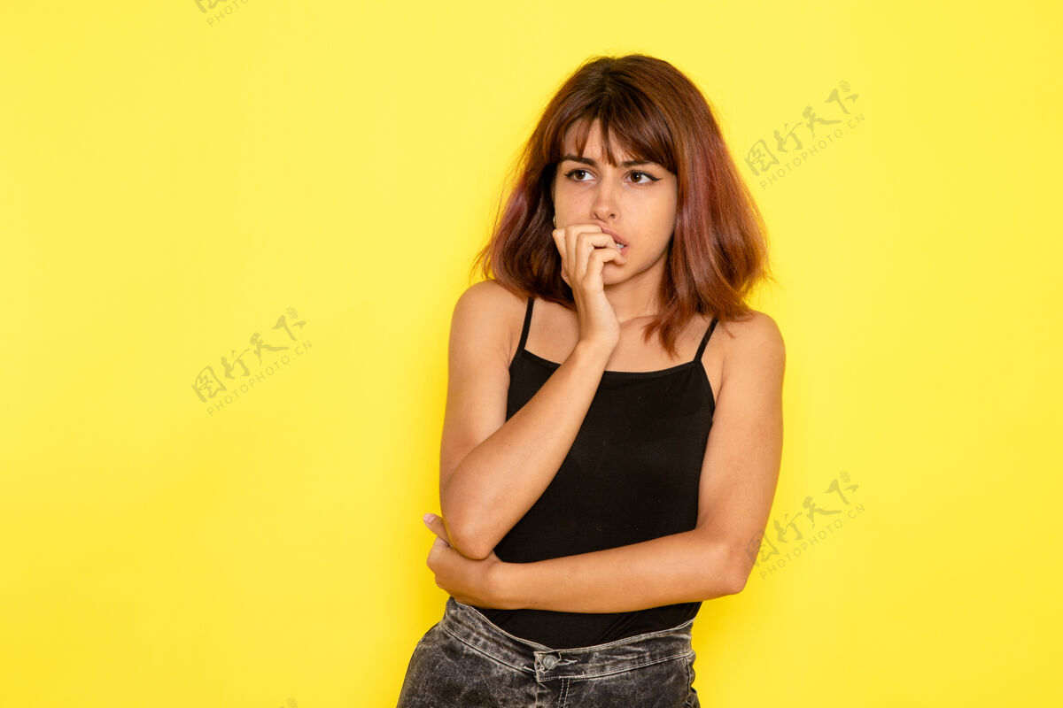 漂亮前视图中的年轻女性穿着黑色衬衫 在黄色的墙上摆出困惑的表情头发女孩时尚