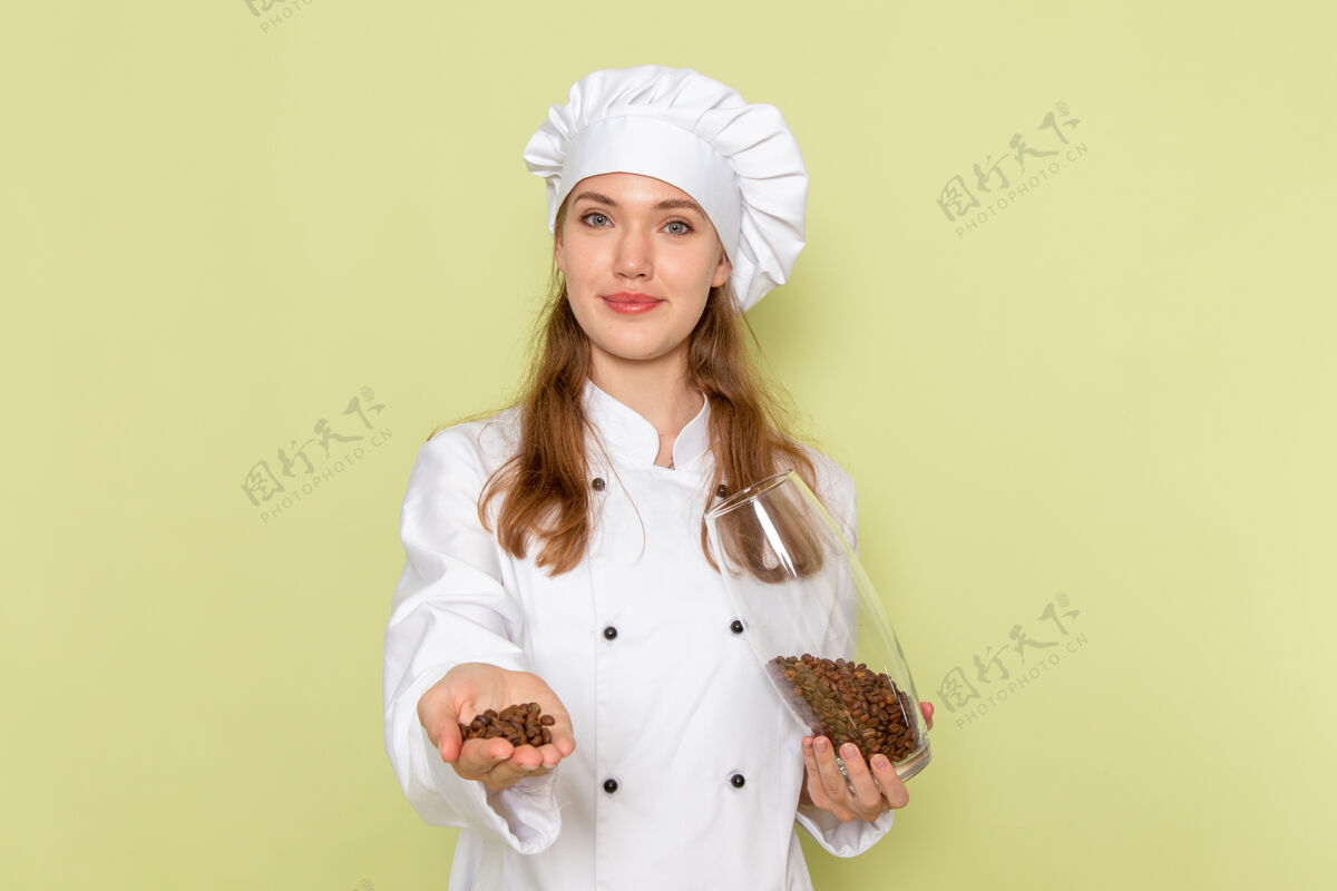 膳食身着白色厨师服的女厨师正拿着装满咖啡籽的罐子站在浅绿色的墙上咖啡女厨师医生