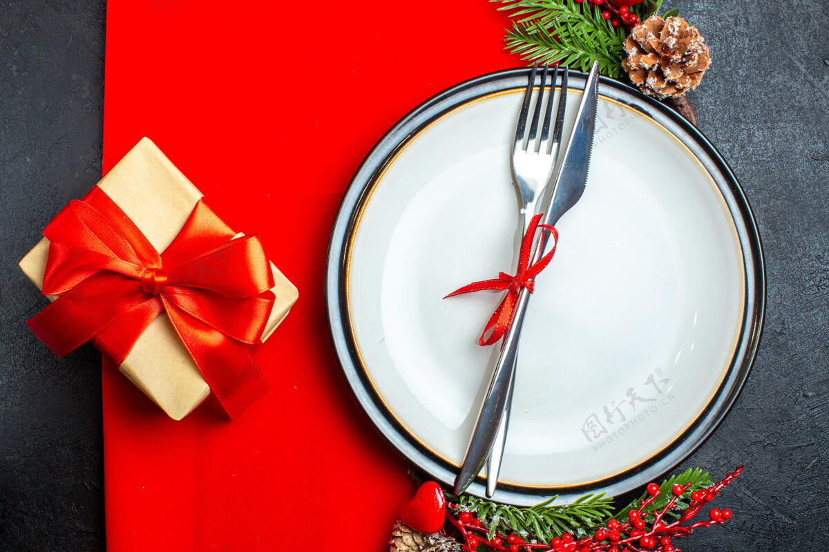 餐巾xsmas背景顶视图 餐具套装 餐盘上有红丝带装饰配件杉木树枝 旁边有一件礼物 放在红色餐巾上圣诞上衣餐盘