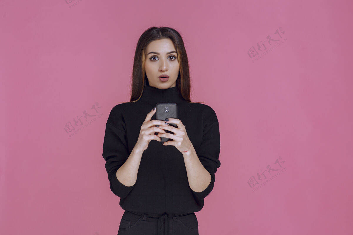 聊天穿着黑色毛衣的女人拿着智能手机发短信或查看社交媒体年轻移动小工具