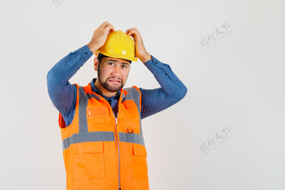 背心年轻的建筑工人手牵着手 头上穿着衬衫 背心 头盔 神情无助 俯瞰前方职业工业工人