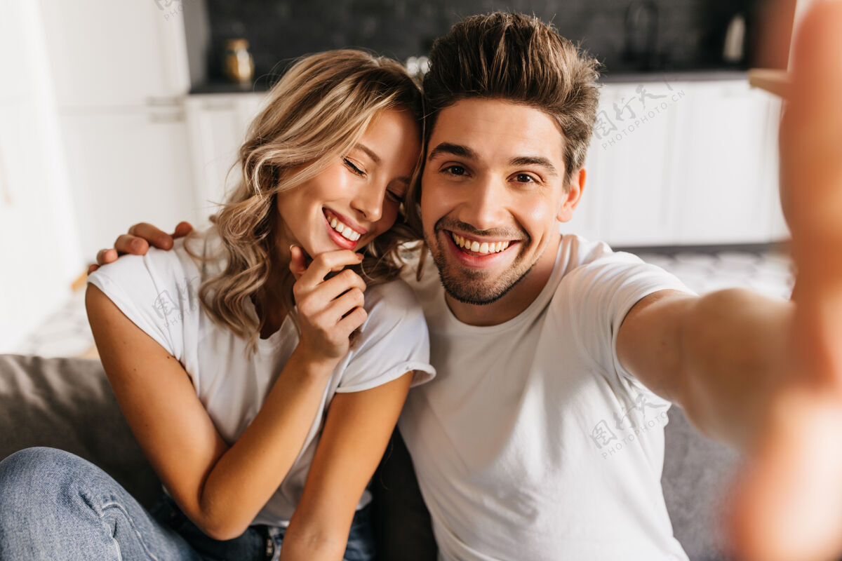 家一对浪漫的笑脸情侣坐在沙发上在家里自拍男人和他的女朋友开心地闭着眼睛微笑肖像情人拥抱