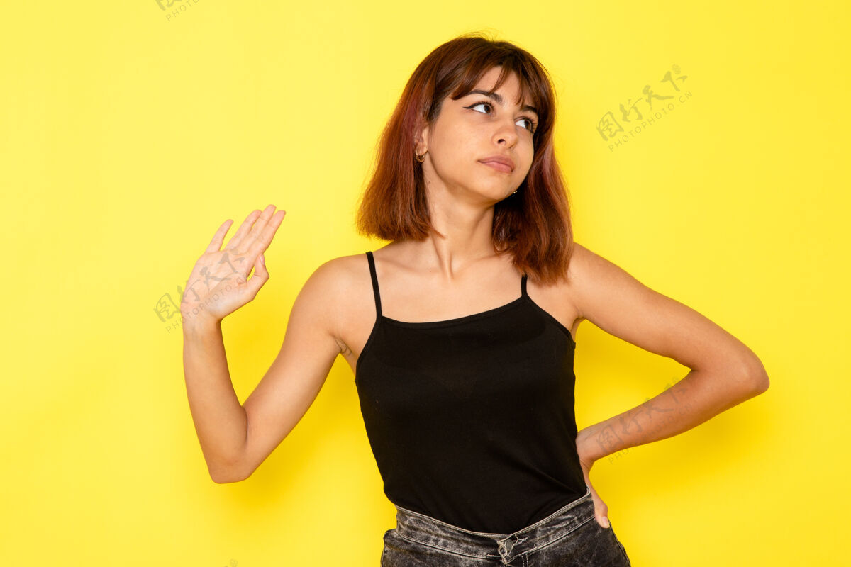 模特身穿黑色衬衫和灰色牛仔裤的年轻女性在黄色墙壁上简单地摆姿势情感简单性感