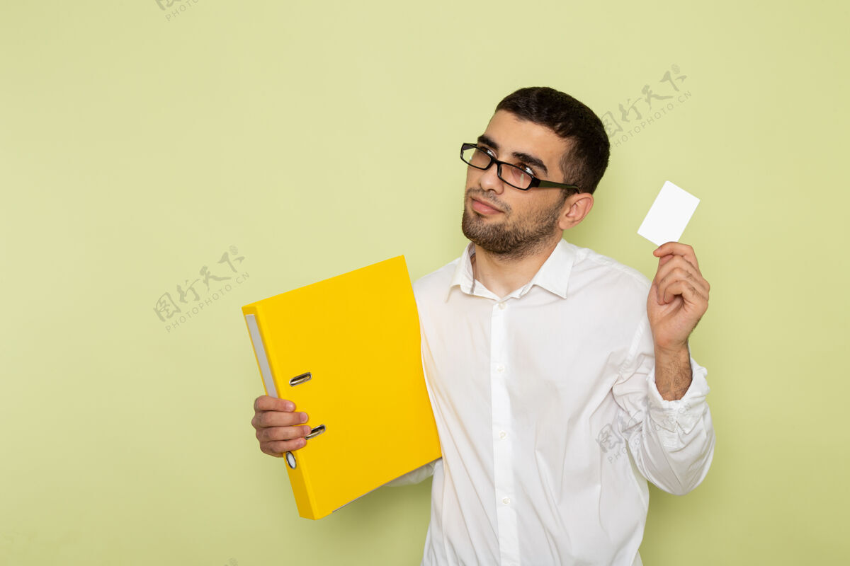 衬衫身穿白衬衫的男办公室工作人员正拿着卡片和绿色墙上的文件前面男性成人