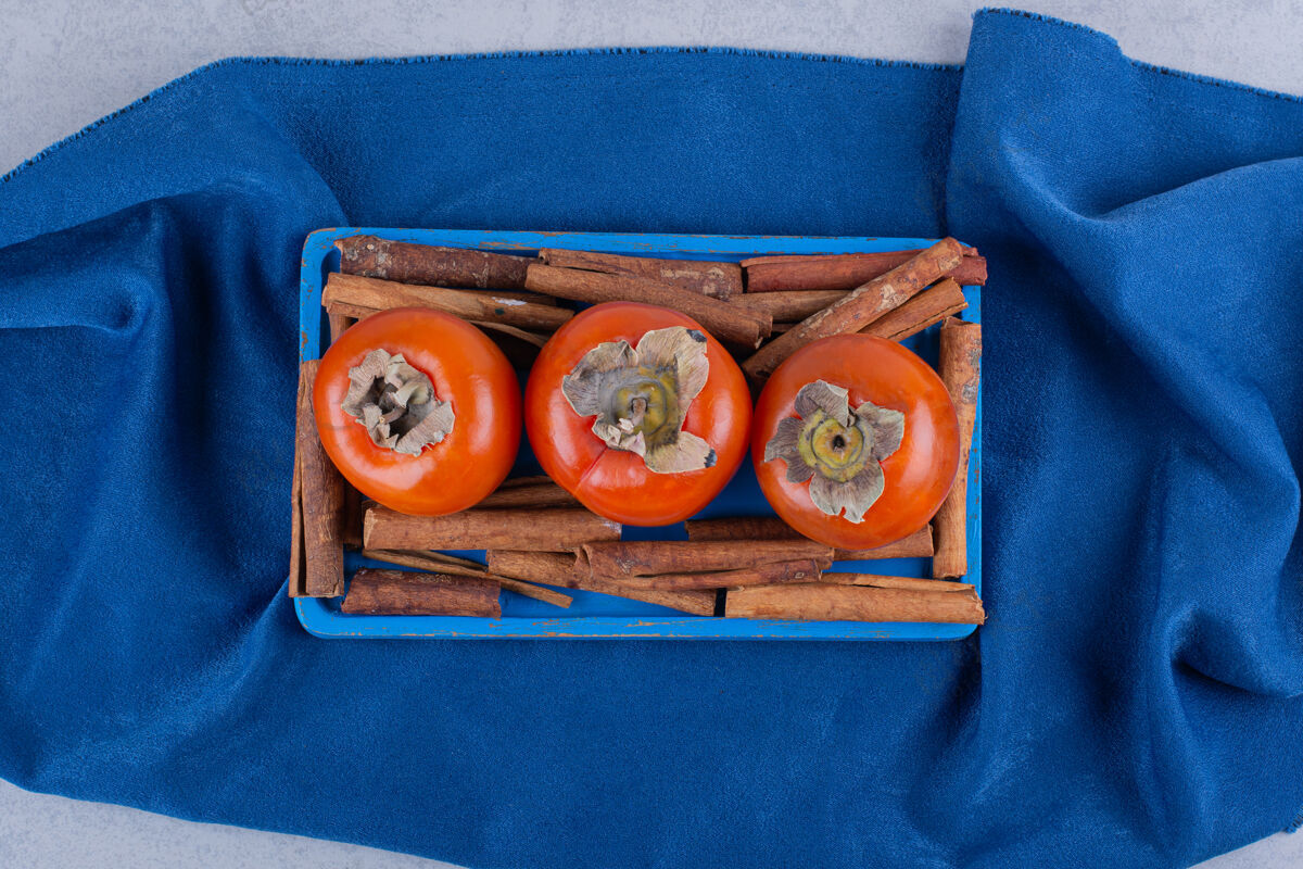 健康新鲜柿子和肉桂条放在蓝色盘子里新鲜营养食用