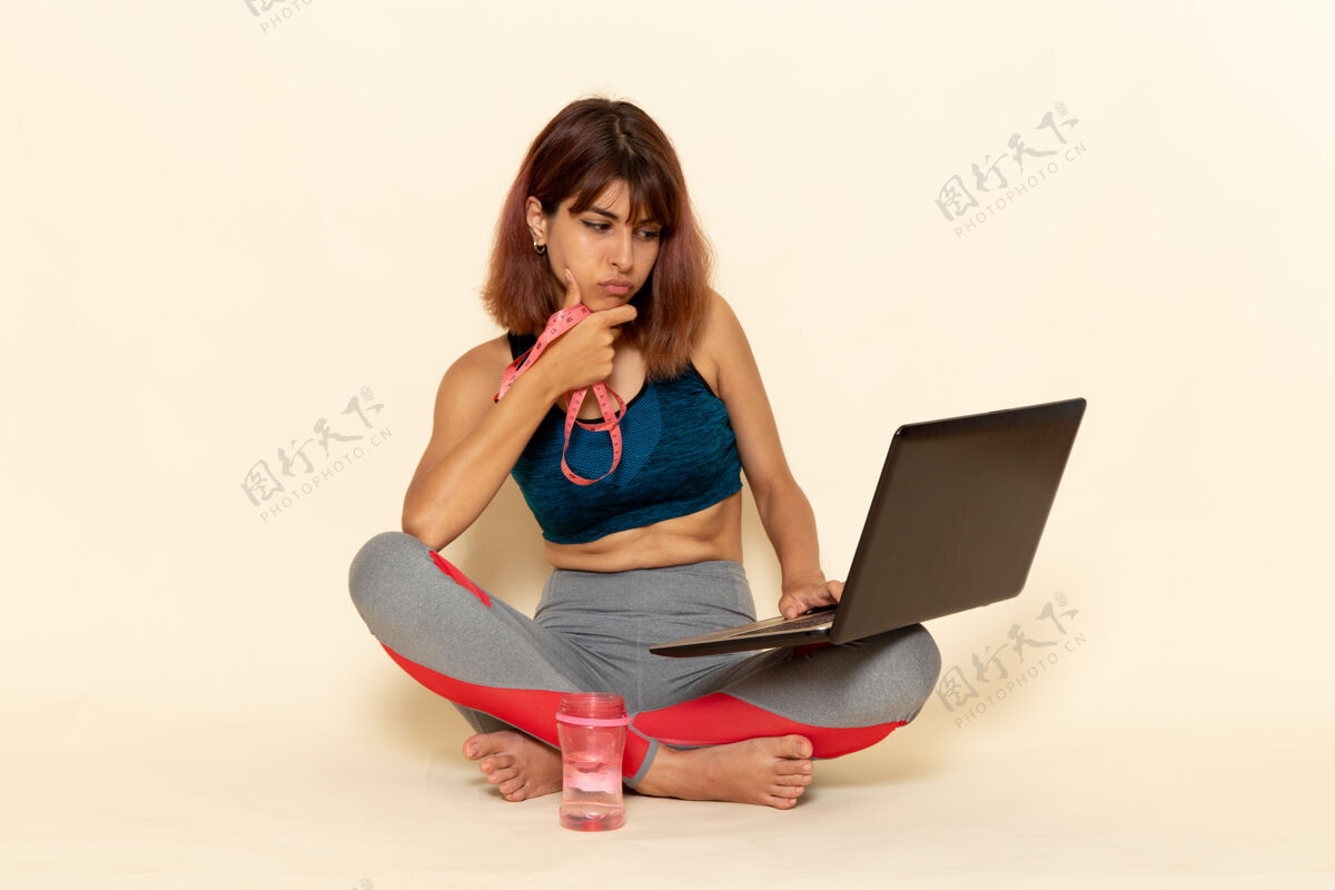私人教练穿着蓝色衬衫 身体健康的年轻女性在浅白墙上使用笔记本电脑的前视图运动身体年轻人