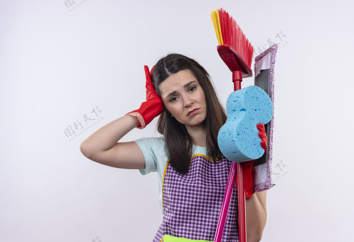 围裙穿着围裙 戴着橡胶手套 拿着清洁工具的年轻漂亮女孩看起来很累 而且工作过度 头痛清洁橡胶抱