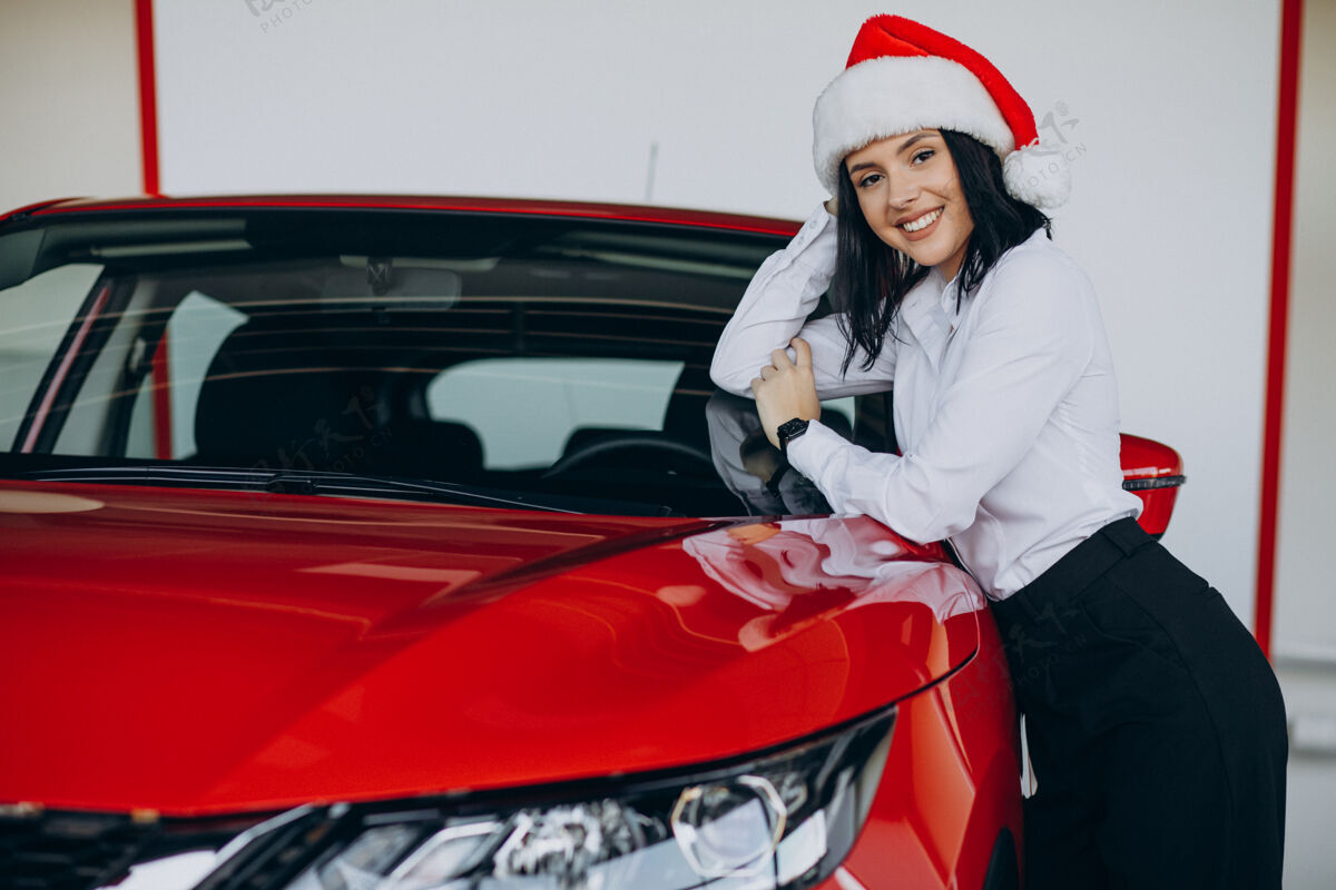 情感一个戴着圣诞帽的女人坐在汽车陈列室里的红色汽车旁边购买选择节日