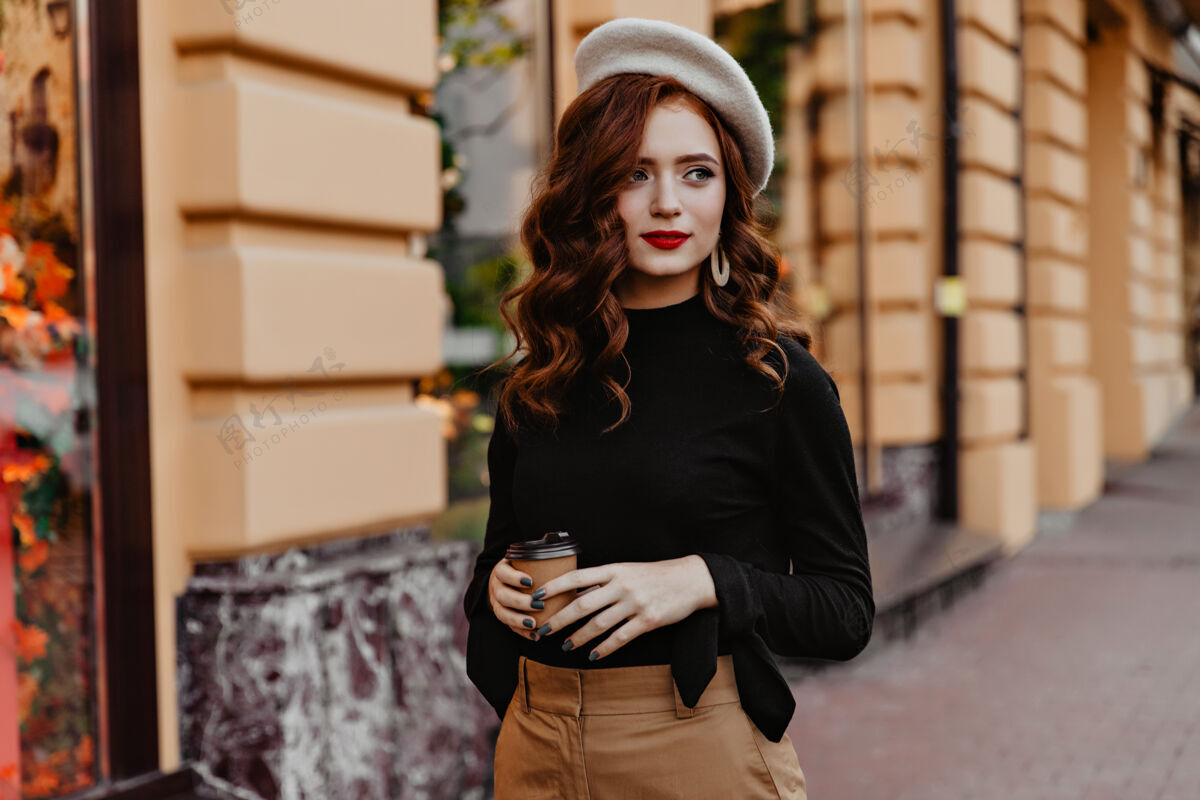 卡布奇诺一位漂亮的法国女士拿着一杯咖啡四处张望一个穿着黑色上衣的忧郁的卷发女孩走在街上城市法国严肃