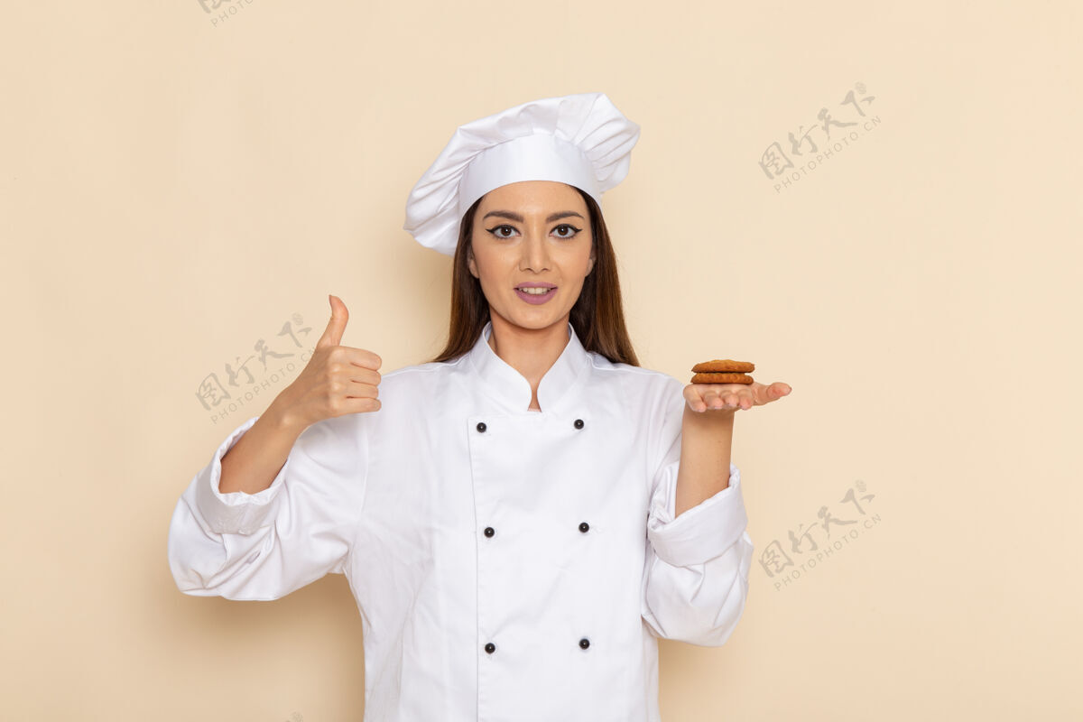 工作身穿白色厨师服的年轻女厨师正拿着饼干站在浅白的墙上人制服专业