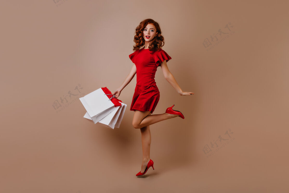 姜黄色身材苗条的购物狂女孩的全身肖像穿着红色连衣裙的长发女人惊讶地跳起来纸女人欢乐