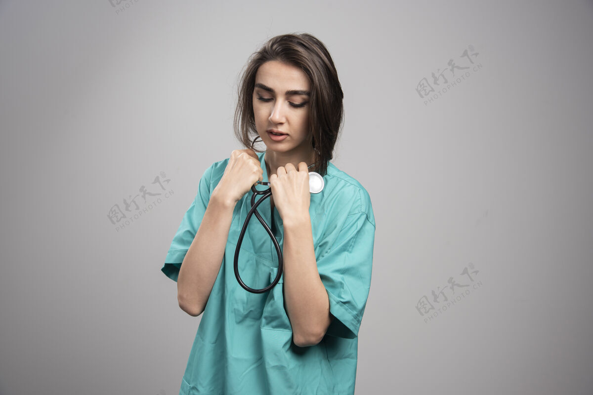检查年轻的医生穿着制服在灰色的墙上用听诊器成人女性医院
