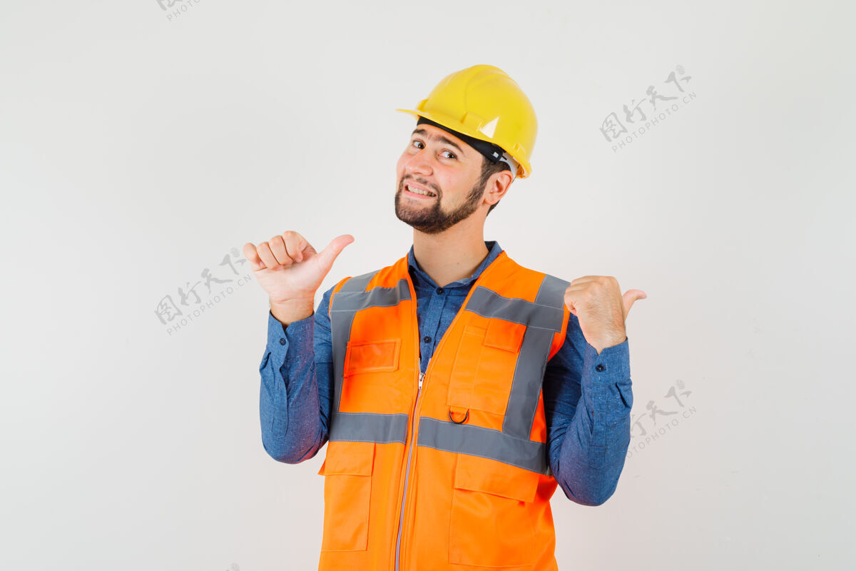 工人年轻的建筑工人穿着衬衫 背心 头盔 拇指向后指 看上去很快乐前视图制服工作前面