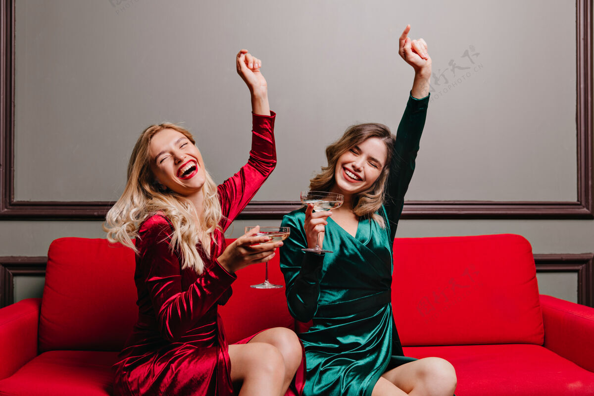 成人穿着天鹅绒衣服喝葡萄酒的快乐女孩迷人的女士坐在沙发上喝香槟的室内肖像室内沙发香槟