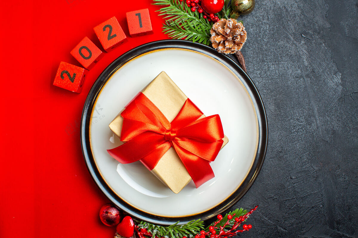 圣诞新年背景的顶视图 餐盘上有礼物装饰配件杉木树枝和数字 在黑色桌子上的红色餐巾上顶部树枝蝴蝶结