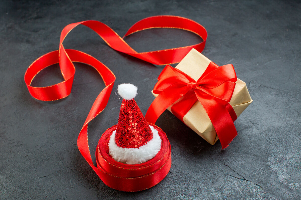 圣诞老人帽子俯瞰圣诞老人帽子上的一卷丝带和美丽的礼物在黑暗的背景鞠躬头顶圣诞节