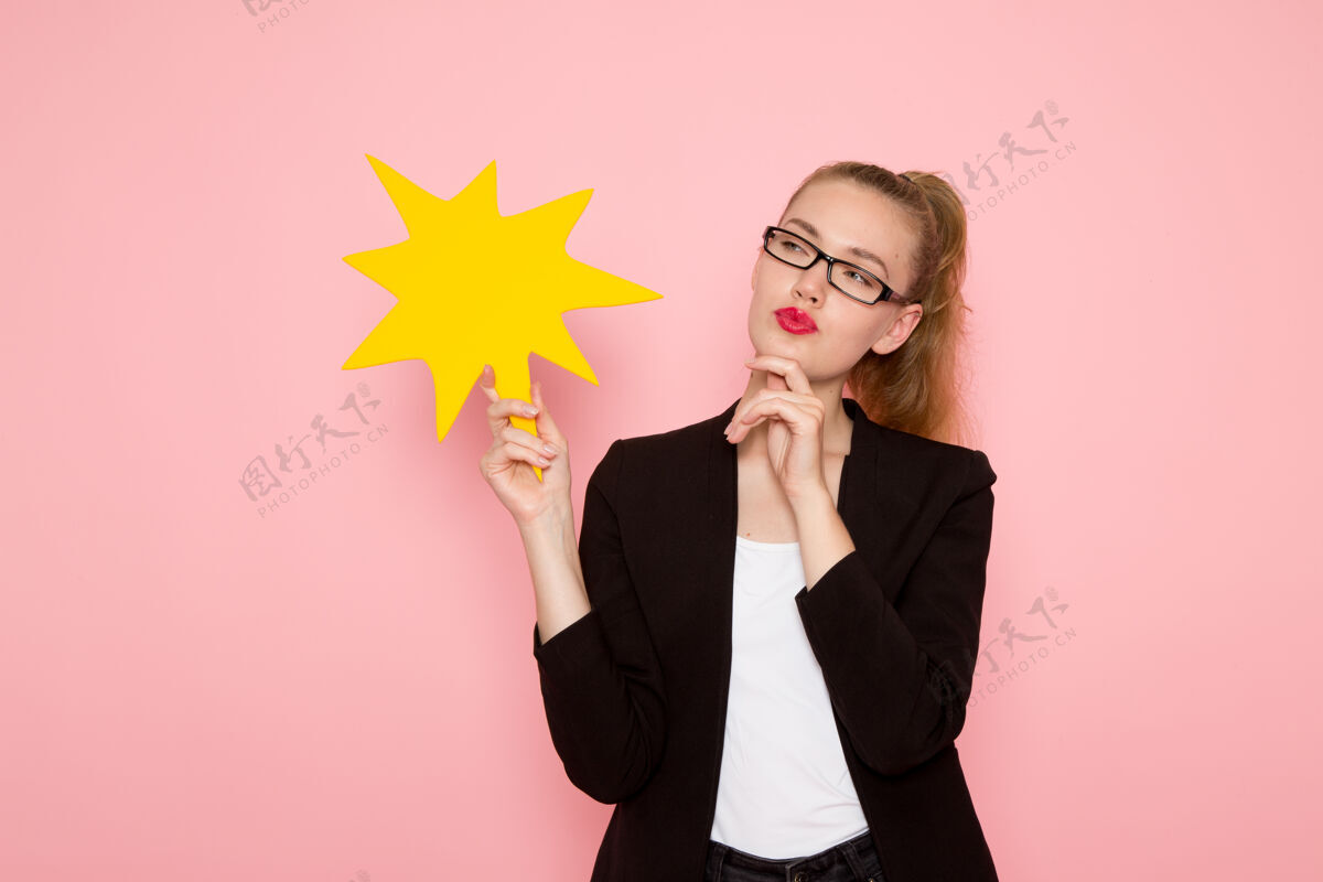 思考身穿黑色紧身夹克 手持黄色标牌 在粉色墙上思考的女上班族正面图持有商业女性夹克